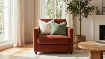 Rust accent chair styled with cream and sage green throw pillows in a cozy modern living room