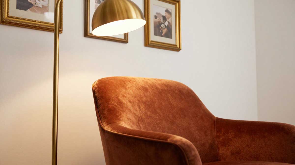 A luxury brushed brass floor lamp casting warm ambient lighting over a plush rust velvet accent armchair.