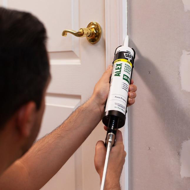 A continuous bead of paintable caulk being applied along a narrow joint between door casing and drywall.