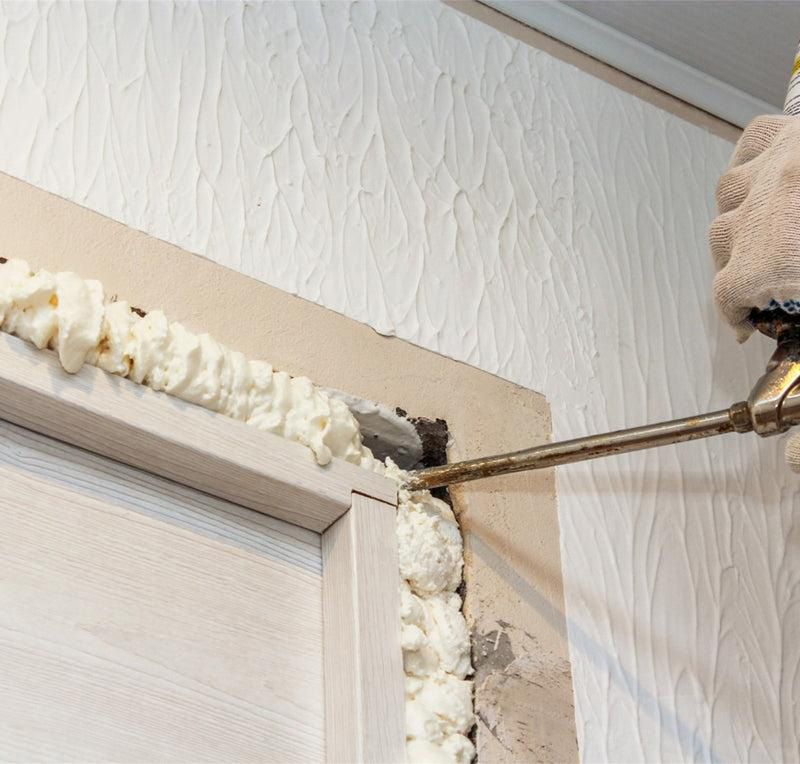 A small, controlled amount of door-and-window foam in the gap between a door jamb and a rough wall opening with the casing removed.
